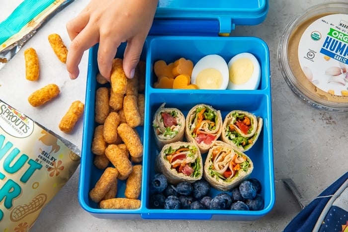Child's hand reaching into a bento lunchbox filled with vegetarian snacks
