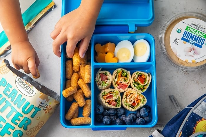 Children's hands reaching for food in vegetarian bento lunchbox
